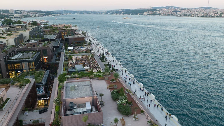 Aerial view of the waterfrom promenade of the Galataport in Istanbul, with modern buildings and people by a wide strait at dusk.