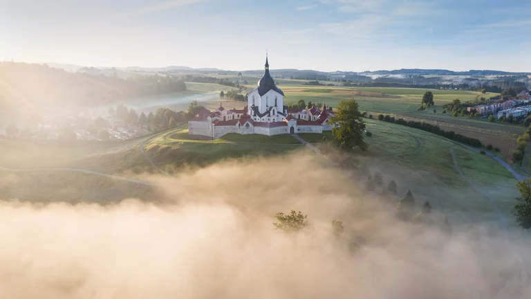 Aerial view of Žďár nad Sáazavou Zelena Hora church on a hill surrounded by morning mist at sunrise.