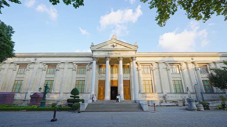 Classical building with columns and steps, adorned with sculptures and surrounded by greenery.
