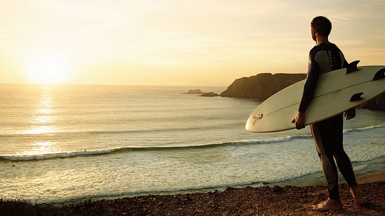 Surfer with a board looking at the sea during sunset.