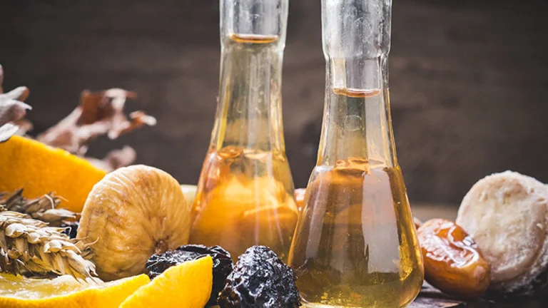 Two glass flasks with amber rakija among dried fruits and nuts on a wooden surface.