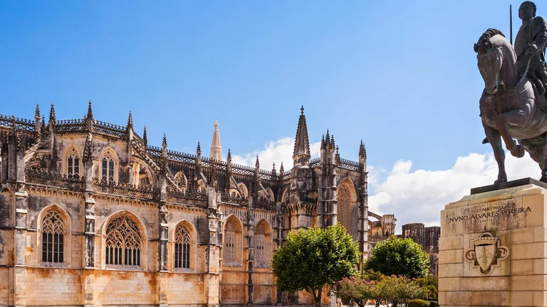 The Batalha Monastery in Portugal, a masterpiece of Gothic architecture, featuring intricate details and a statue of Nuno Álvares Pereira in the foreground.