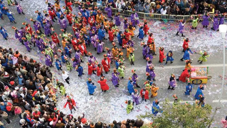 A Carnival parade in Limassol, Cyprus, with costumed participants and confetti-covered streets, viewed from above.