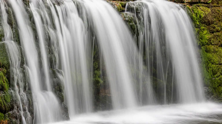 A serene waterfall with silky cascades flowing over mossy rocks.