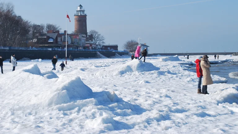 People enjoying a snowy landscape near a lighthouse on a clear day.