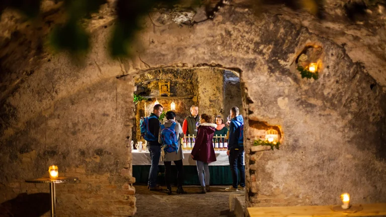 Group of people in the candlelit underground Tokaj cellar with stone walls.