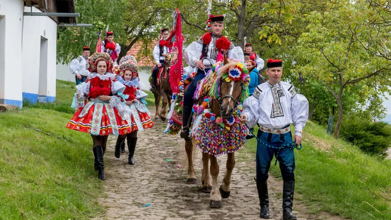 People in traditional outfits walking alongside decorated horses on a cobblestone path.