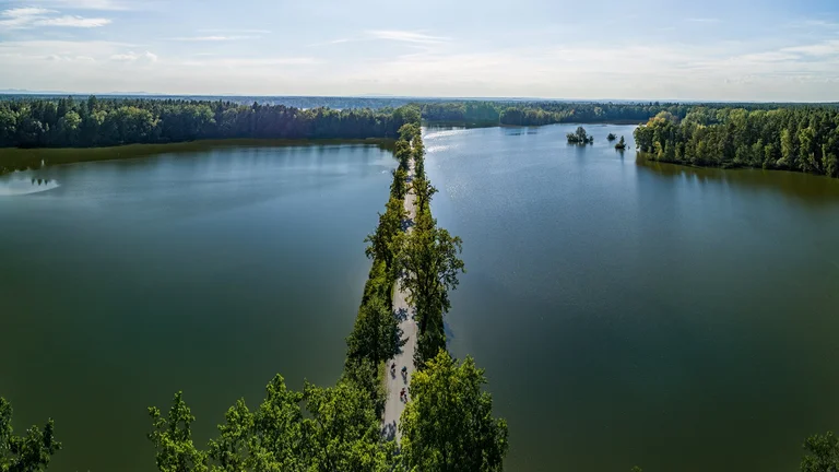 Aerial view of a narrow tree-lined pathway separating two tranquil lakes under a clear sky.