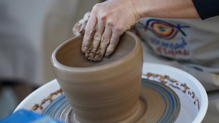 A close-up of a hand shaping wet clay on a potter's wheel, crafting a brown pottery bowl.