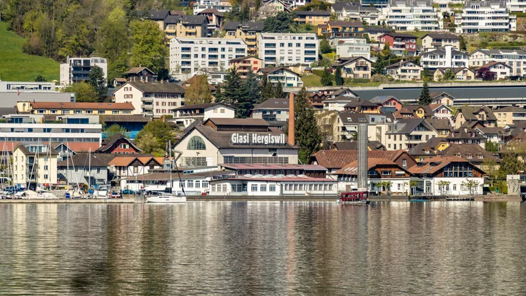 A picturesque view of Hergiswil, Switzerland, featuring the Glasi Hergiswil glass factory amid colorful hillside homes and a marina.