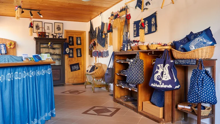 The interior of a charming shop displaying blue textile products, including bags, pillows, and wall hangings, with wooden accents and decor.