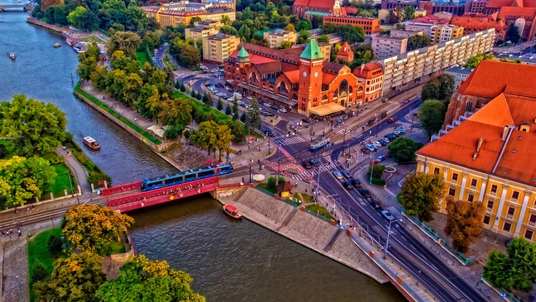 Aerial view of Wrocław featuring a river, bridges, green parks, and historic buildings at sunset.