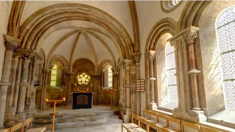 A serene chapel interior with vaulted arches, stone columns, and stained glass windows casting patterned light.