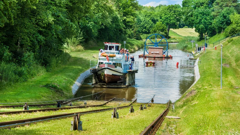A boat entering the water section of the Elbląg Canal, surrounded by lush green landscape.