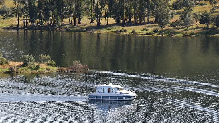 Small leisure boat cruising on Alqueva Lake surrounded by forest.