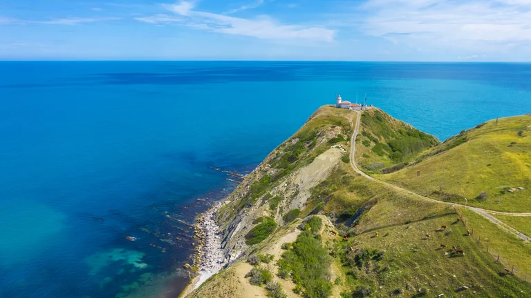 Cape with a lighthouse overlooking turquoise sea.