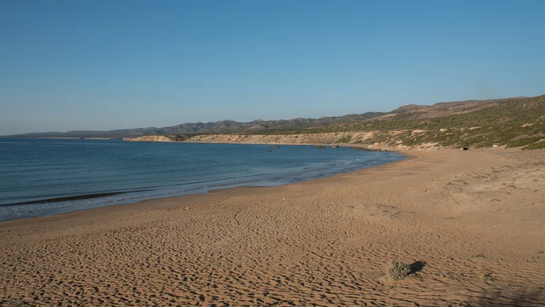 A wide, empty stretch of golden sand at Lara Beach, with gentle waves and rugged hills in the distance.