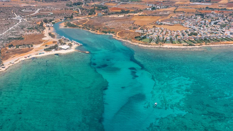 Aerial view of Liopetri River flowing into the sea, with crystal-clear turquoise water, golden coastline, and nearby residential areas.