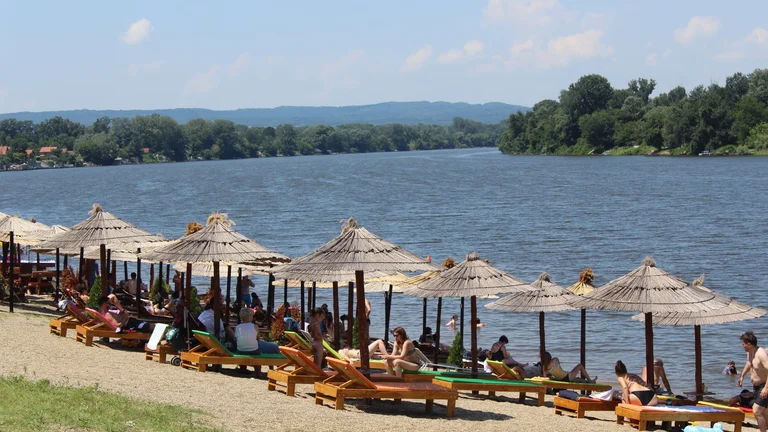 People relaxing on sunbeds under straw umbrellas by Silver Lake beach.