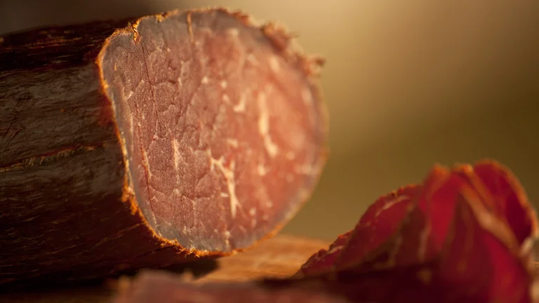 Close-up of Serbian smoked cured ham, showing its deep color and texture with slices cut.