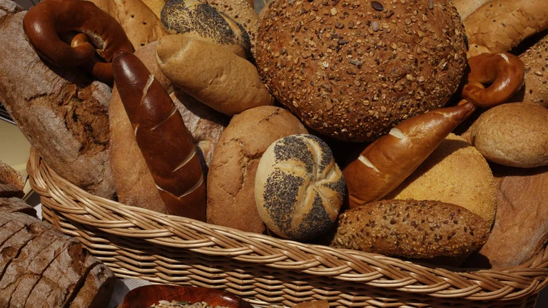 Assortment of traditional Serbian breads, from rustic loaves to pretzels and seeded rolls, in a woven basket.