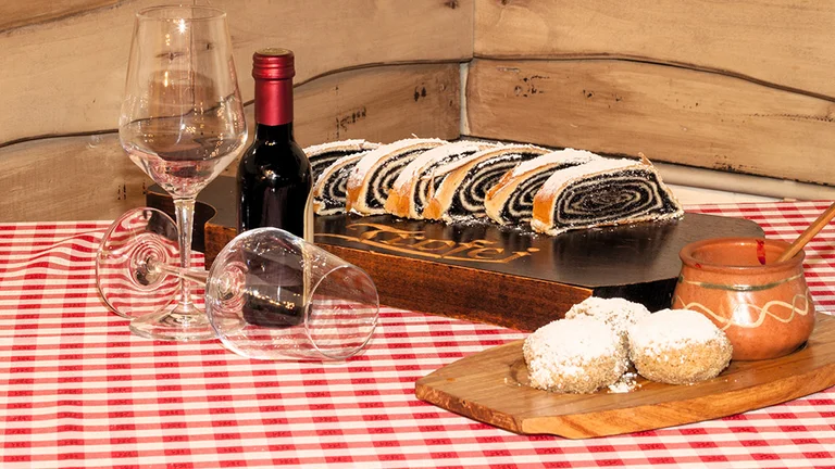 Traditional Serbian walnut roll cake and dumplings dusted with sugar, served with wine on a red-checkered tablecloth.