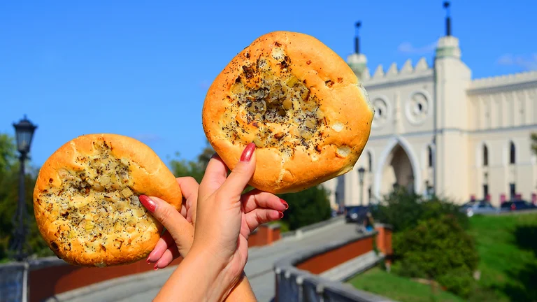 A woman’s hand holding two Polish cebularze with a castle in the background on a sunny day.