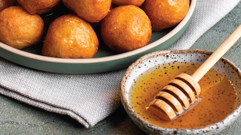 A plate of golden Cypriot loukoumades, small fried dough balls, accompanied by a dish of honey.