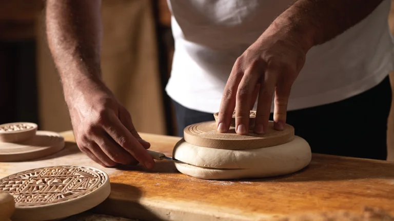 A man preparing traditional Cypriot bread, cutting the dough into its characteristic form before baking.