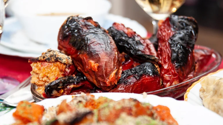 Traditional Bulgarian stuffed peppers filled with rice and vegetables, roasted until charred, served as part of a festive Christmas dinner with wine and side dishes.