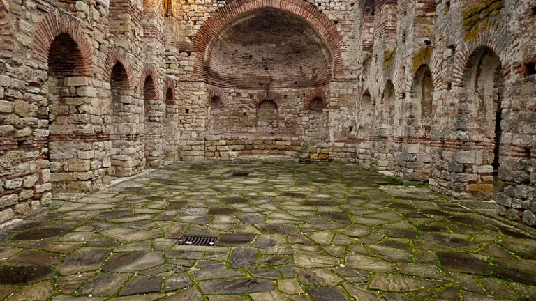 Interior view of the Byzantine Church of Old Nessebar, with stone arches and open roof, as a purple sky glows through at sunset.