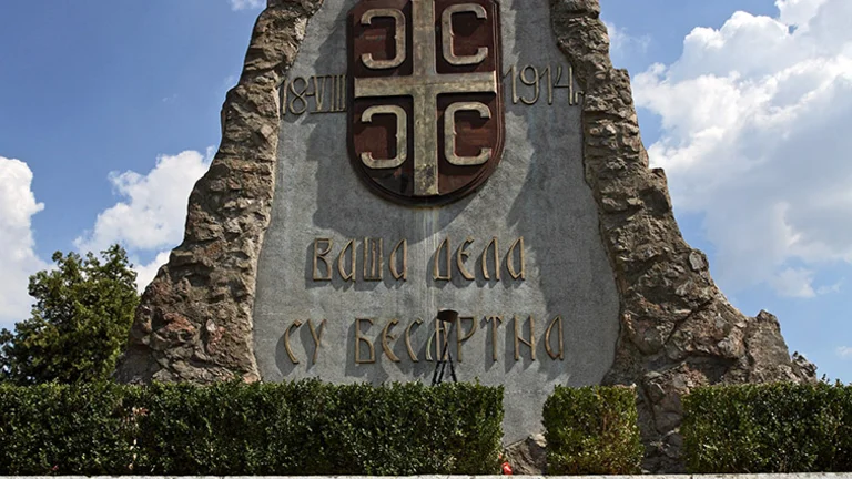 A tall, pyramid-shaped war memorial made of rough-hewn stone, set against a bright blue sky with scattered white clouds