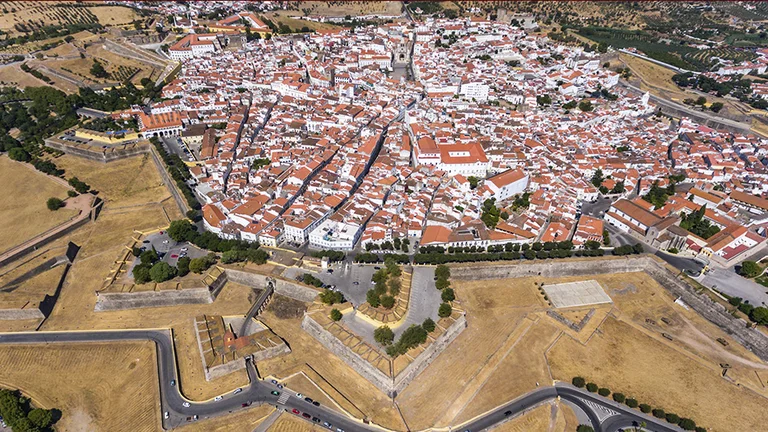Bird’s-eye view of Elvas, Portugal, featuring clusters of white houses with orange-tiled roofs surrounded by fields and open countryside.