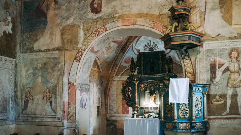 Interior of the Gothic church in Kraskovo, Slovakia, featuring medieval frescoes and a sacred scene painted on the historic walls.