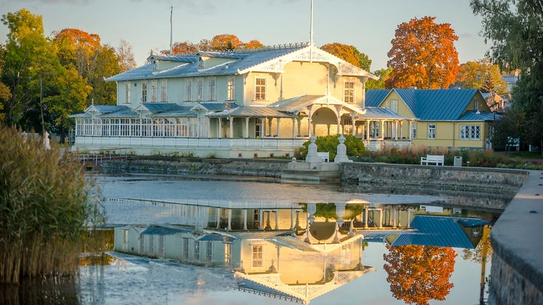 Ornate wooden lacework of Haapsalu’s Kuursaal in autumn orange hues, reflected in the calm lake waters in front.