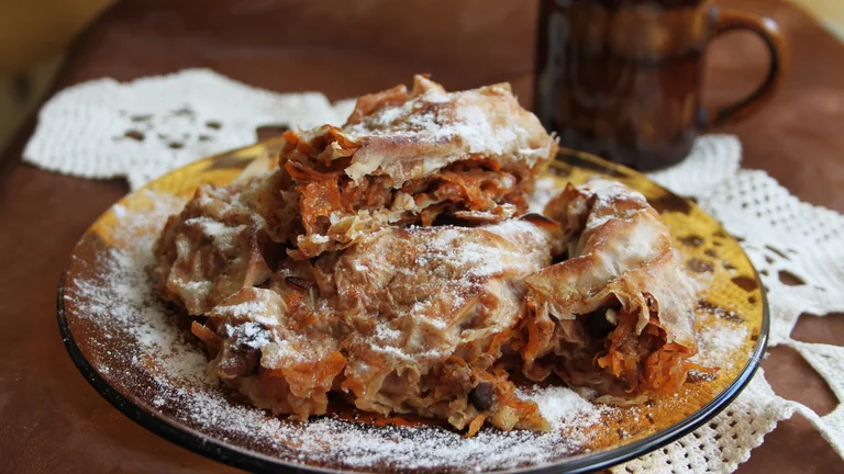 Traditional Bulgarian pumpkin pastry, known as tikvenik, made with layers of phyllo dough, sweet pumpkin, walnuts, and cinnamon, dusted with powdered sugar.