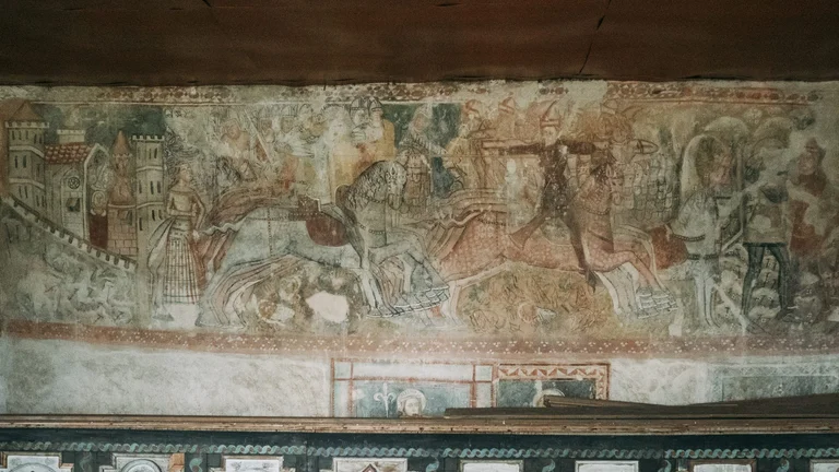 Interior of the Gothic church in Rimavská Baňa, Slovakia, featuring medieval frescoes, ribbed vaults, and soft light illuminating the painted walls.