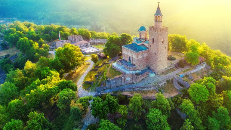 Tsarevets Fortress in Veliko Tarnovo, Bulgaria, perched on a hilltop with stone walls, towers, and a church, surrounded by greenery