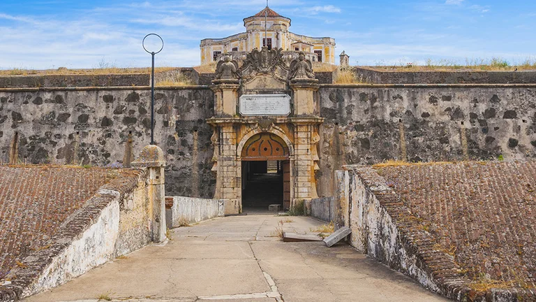 "Front view of the Graça Fortress in Elvas, showing its dense stone walls under a bright blue sky.