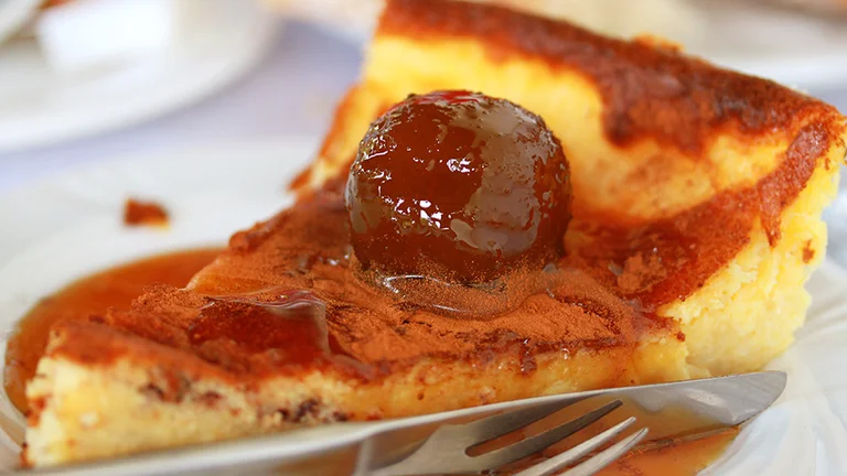 Close-up of Sericaia Ameixa, a traditional Portuguese dessert from Elvas, featuring creamy custard topped with plums and dusted with cinnamon.