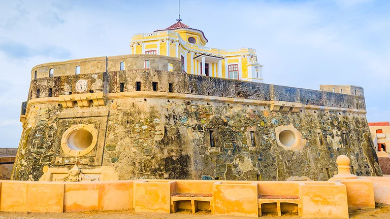 Aerial photo of Graça Fortress in Elvas, Portugal, showing dense stone structures with yellowish tones under a bright blue sky.