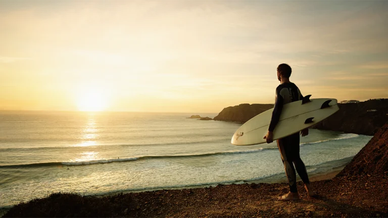 ポルトガルのアルガルヴェ地方、アリファナ海岸の砂浜に立つサーファー。背後には崖があり、波は見えない。