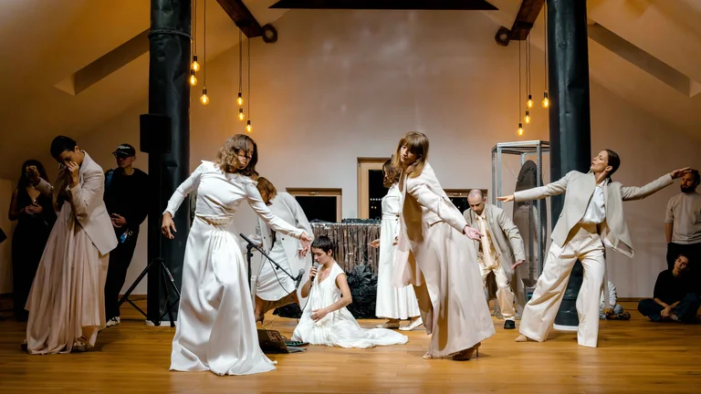 Performance de danse contemporaine dans un loft, avec des interprètes vêtus de vêtements blancs et crème, entourés d’une scénographie minimaliste.