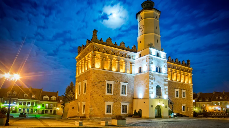 Illuminated historic town hall with a tall clock tower under a moonlit night sky