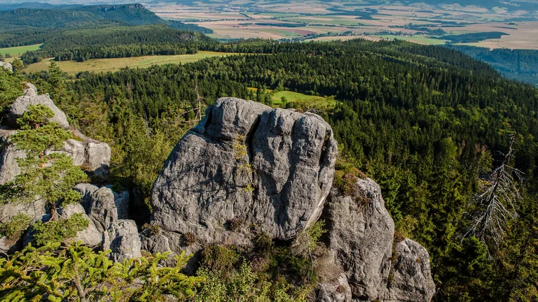 Large gray rock formations surrounded by dense green forest and distant fields.
