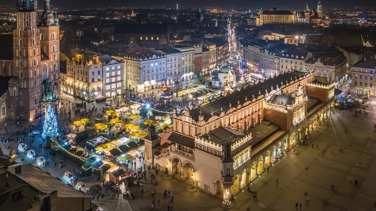 Aerial night view of a historic European market square with a long arcade building and Christmas market stalls
