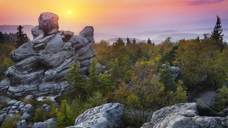Rocky outcrop surrounded by trees at sunset, with a colorful sky in the background.