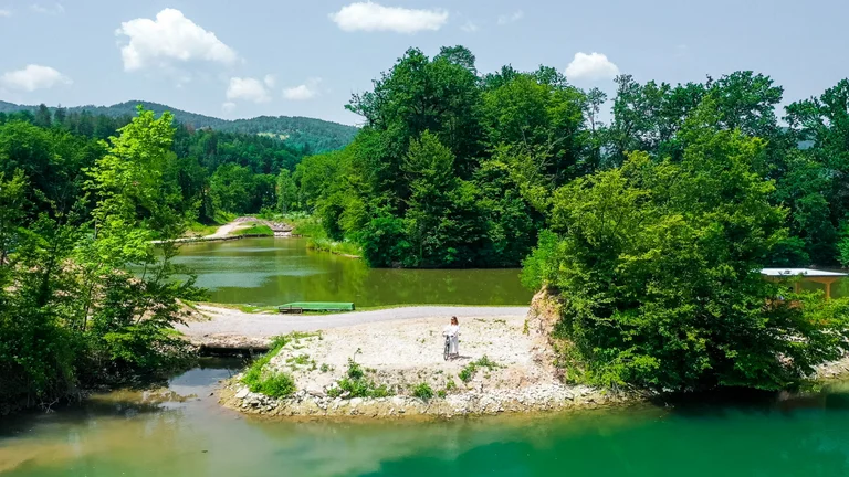Scenic view of the Sava River surrounded by lush green forests, with a person cycling along the riverbank