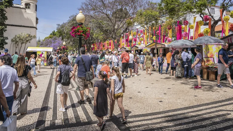 Crowd walking through a lively outdoor market with colorful decorations and vendor stalls.