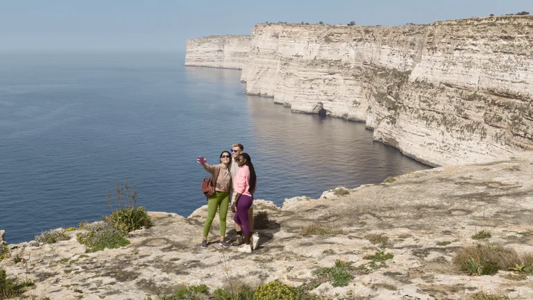 Three people taking a selfie on a rocky cliff overlooking the sea and limestone cliffs.